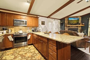 Warm and inviting, this open-concept living space features a fully equipped kitchen, a cozy stone fireplace, and charming wood-beam ceilings—perfect for gathering with loved ones or enjoying a quiet evening in.