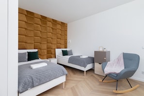 Modern bedroom with two single beds, desk with chair, rocking chair, cabinets and closet.