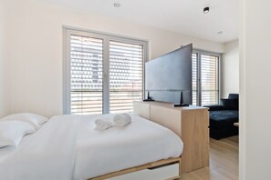 Stylish bedroom featuring a wall-mounted TV and a window that ushers in the morning sun.