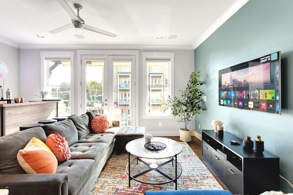 A cozy living room with a beige couch, coffee table, and ceiling fan. The couch is facing the coffee table, suggesting that it is a space for people to gather and relax. The ceiling fan provides a cooling breeze, making the room feel comfortable and inviting. The natural light streaming through the windows illuminates the space, creating a warm and inviting atmosphere.