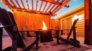 Pergola-covered patio with Adirondack chairs, fire table, and gas grill.