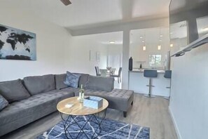 Spacious living room with L-shaped couch, smart TV, open kitchen, dining nook, and patio views (2)