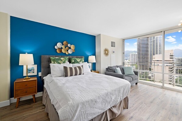Bright studio with a queen bed, cozy sofa, and private balcony offering city views.