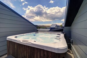 Outdoor hot tub on a rooftop deck between two sloped roofs, with a clear blue sky and scattered clouds in the background.