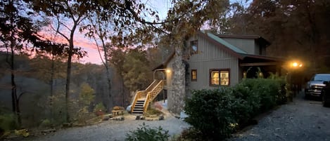 Side view of cabin at dusk. Two parking areas accommodate up to 5 vehicles.