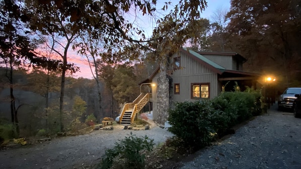 Side view of cabin at dusk. Two parking areas accommodate up to 5 vehicles.