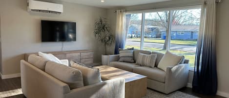 Light filled living room with two comfy couches, media console with games & TV