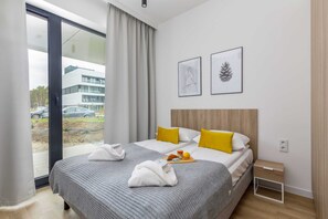A cozy bedroom with a double bed, soft grey bedding, decorative pillows, and minimalistic wall art.