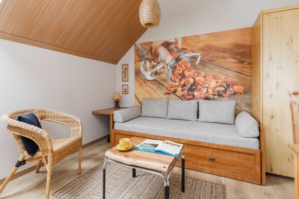 A cozy living space with a wooden sofa, bright cushions, and a rustic vibe complemented by slanted ceilings and natural wood details.