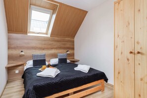 A cozy bedroom with sloped ceilings, a comfortable double bed, and wooden furniture for a natural, warm aesthetic.