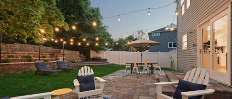 Fenced-in backyard featuring Polywood furniture and café string lights overhead.