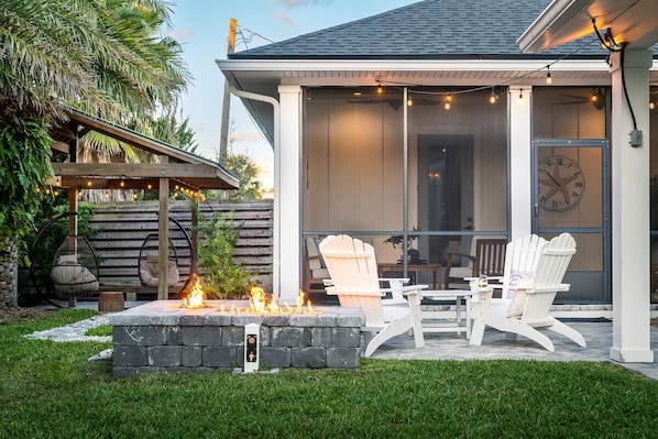 The private backyard features many lounging areas! Shown are sun chairs with a center table, an enclosed lanai with seating and ceiling fans, and a gazebo lit up with overhead lights and swinging chairs.