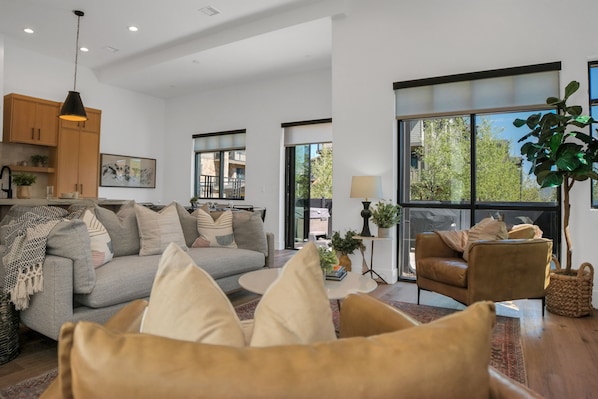 Open floor plan living room with neutral toned furnishings and large windows to the ground.