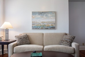 Below the beautiful ocean view painting in the living room is a sofa that pulls out as a sleeper.