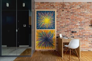 A cozy work desk featuring a brick accent wall and a bold, colorful painting, combining industrial and modern styles.
