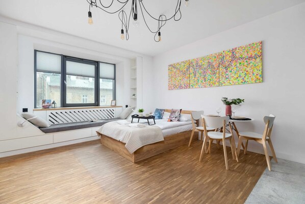 A stylish living room with a large window, bright decor, and vibrant abstract artwork adding a modern touch.
