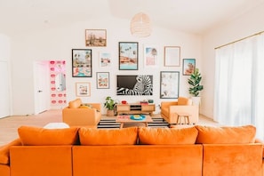 HUGE living room with lots of seating and 80" Samsung FRAME TV in the center. Gallery wall with iconic desert photos. Selfie wall to the left.