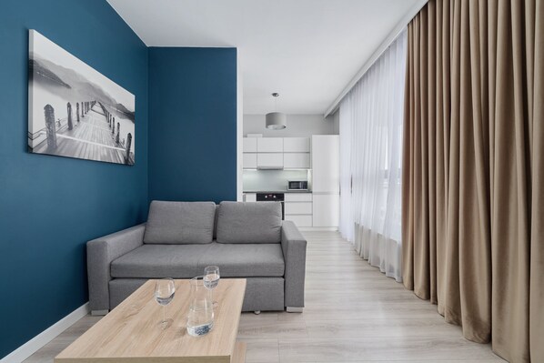 A stylish living room featuring a gray sofa, a wooden coffee table, and a striking blue accent wall, offering a modern and cozy vibe.
