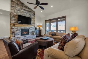 The centerpiece of the living room is the giant stone fireplace, topped by a mounted TV and surrounded by plush, cozy couches to lounge in.