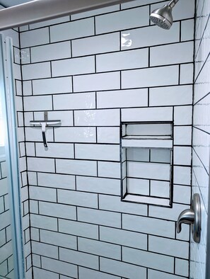 Tiled shower and lighted mirror in bathroom with towels and hair dryer. 