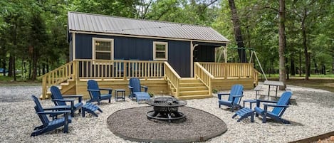 Cottage exterior with deck overlooking a spacious firepit area with ample seating.