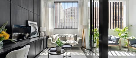 Open plan living space with work desk, leading to covered balcony with armchairs