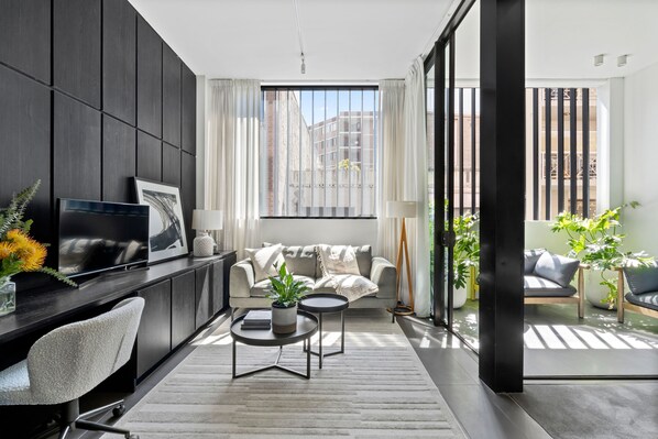 Open plan living space with work desk, leading to covered balcony with armchairs