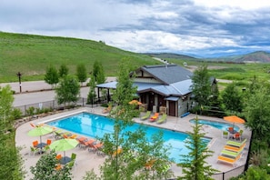 Outdoor swimming pool area with colorful lounge chairs and umbrellas surrounded by greenery