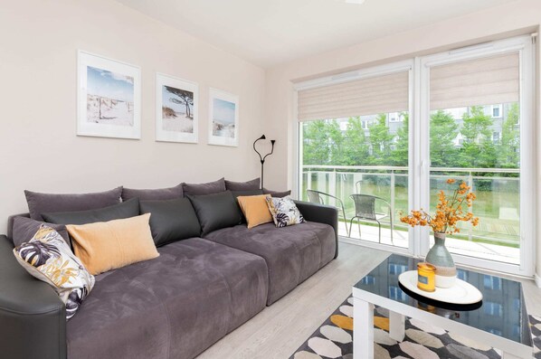A modern and comfortable living area featuring a gray sofa, large windows allowing plenty of natural light, and a simple coffee table.