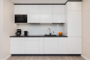 A modern, minimalist kitchen with white cabinetry, black countertops, and plenty of storage space.