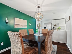 Gather for meals or game nights in this stylish dining area featuring a bold green accent wall, woven chairs, and warm lighting 🍽️🌿 The open layout flows seamlessly into the modern kitchen for easy entertaining!