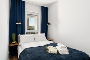 A compact bedroom with a comfortable bed, dark blue bedding, and soft lighting, creating a relaxing atmosphere.
