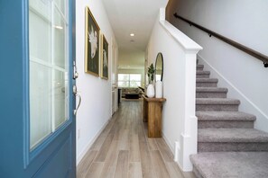 Step into our bright coastal-chic foyer with a welcoming blue door, wood console, round mirror, pelican art, and plush carpeted stairs-a stylish start to your home-away-from-home!