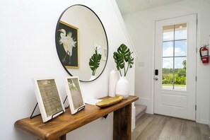 Bright coastal-chic foyer featuring a sleek wood console, oversized round mirror, tropical greenery, and elegant pelican art-your stylish welcome to a serene getaway!
