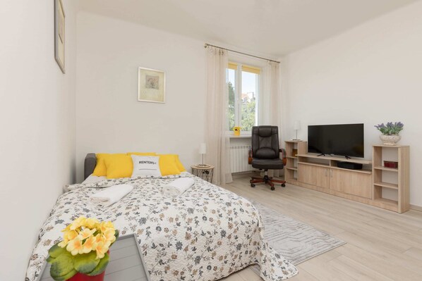 A cozy sleeping space with a double sofa bed, decorated with yellow cushions and floral bedding, with a small desk in the background.