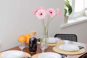 A small dining table set for two, decorated with fresh flowers, oranges, and a juice bottle for a lively atmosphere.