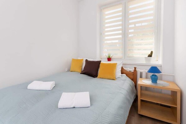 A cozy bedroom featuring a neatly made double bed with turquoise bedding, illuminated by natural sunlight from the window.
