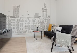 A modern living room featuring a sofa with yellow and gray cushions, a coffee table, and a unique mural of city buildings on the wall.