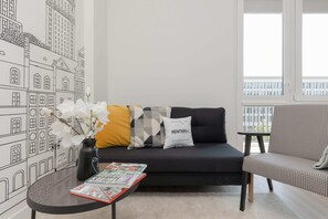 A modern living room featuring a sofa with yellow and gray cushions, a coffee table, and a unique mural of city buildings on the wall.