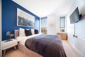 Bedroom 1 offers a double bed measuring 190 x 135 cm (6.2 x 4.4 ft), an ensuite bathroom, wardrobe, mirror, chest of drawers, bedside tables with lamps, a TV with Netflix, and two windows that allow natural light and offerings view of Wembley Stadium