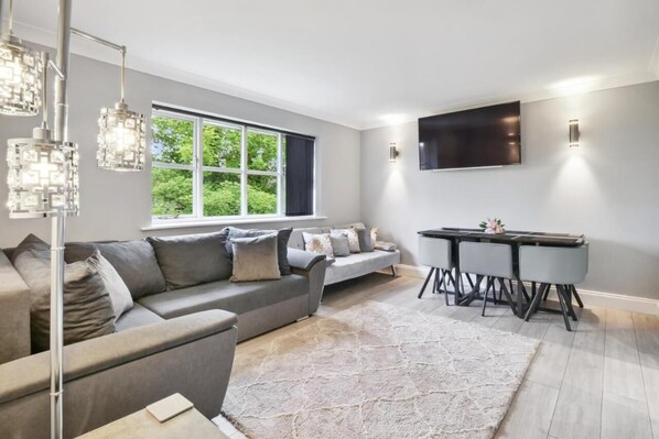 Enjoy the perfect blend of comfort and style in our spacious living room, featuring a sleek flat-screen TV, a welcoming dining table, and a window that fills the room with natural light.
