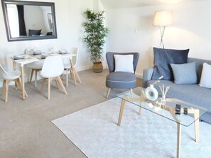 The living room is designed with a perfect blend of comfort and functionality, featuring a stylish sofa bed and a 4-seater dining area.