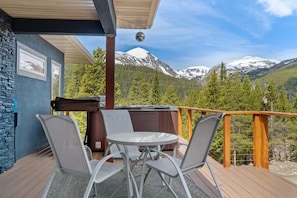 The private outdoor balcony features a hot tub and a patio table with chairs making it a great spot to relax outside and take in the surrounding nature.