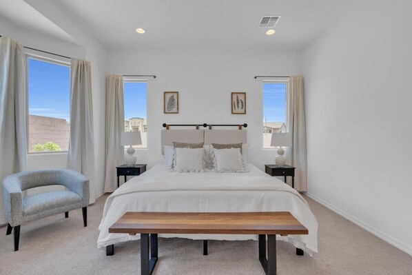 Primary bedroom with king-size bed, comfortable seating, smart TV, dresser, walk-in closet, and en-suite bathroom with soaker tub, double vanity, and walk-in shower