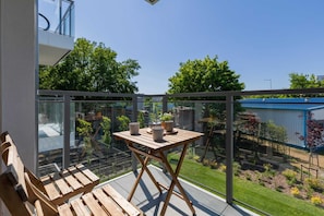 A private balcony with a small table and chairs, overlooking a green space.