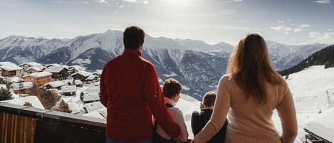 La famille du chalet profite du panorama des montagnes valaisannes depuis le balcon de l'appartement en hiver
