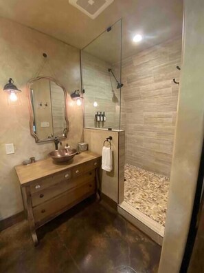 Travertine mosaic with rock border and an antique mirror complete this lavishly appointed bathroom.