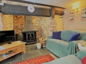 Living room with large log-burner, wooden beams, TV and games.