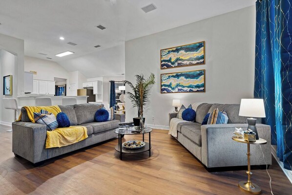 This living room is the epitome of comfy, featuring 2 plush upholstered couches, a coffee table, a 75” HDTV, and a cozy fireplace bringing the ambiance.