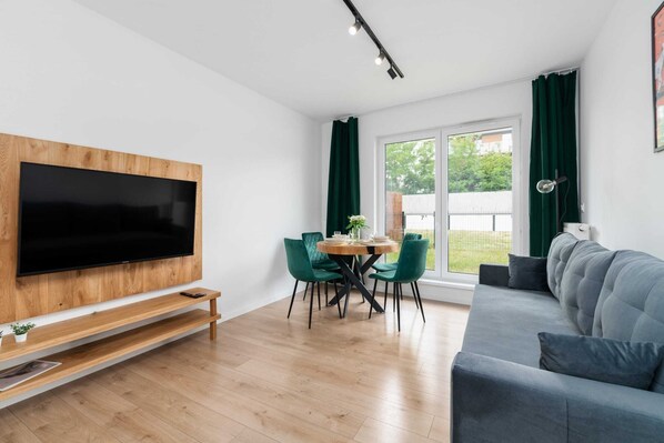 A bright and cozy living room featuring a modern TV unit, a comfortable sofa, and large windows letting in ample natural light.
